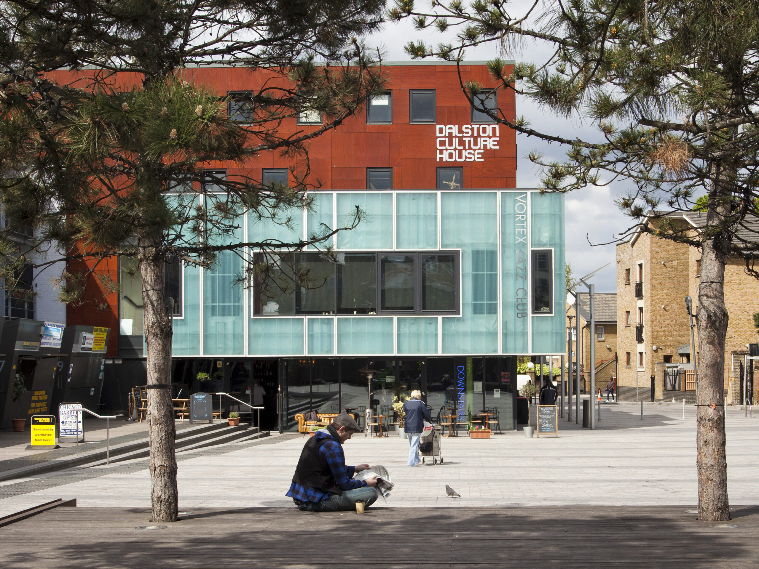 A man reading a newspaper in Gillet square, and another person walking through the square.