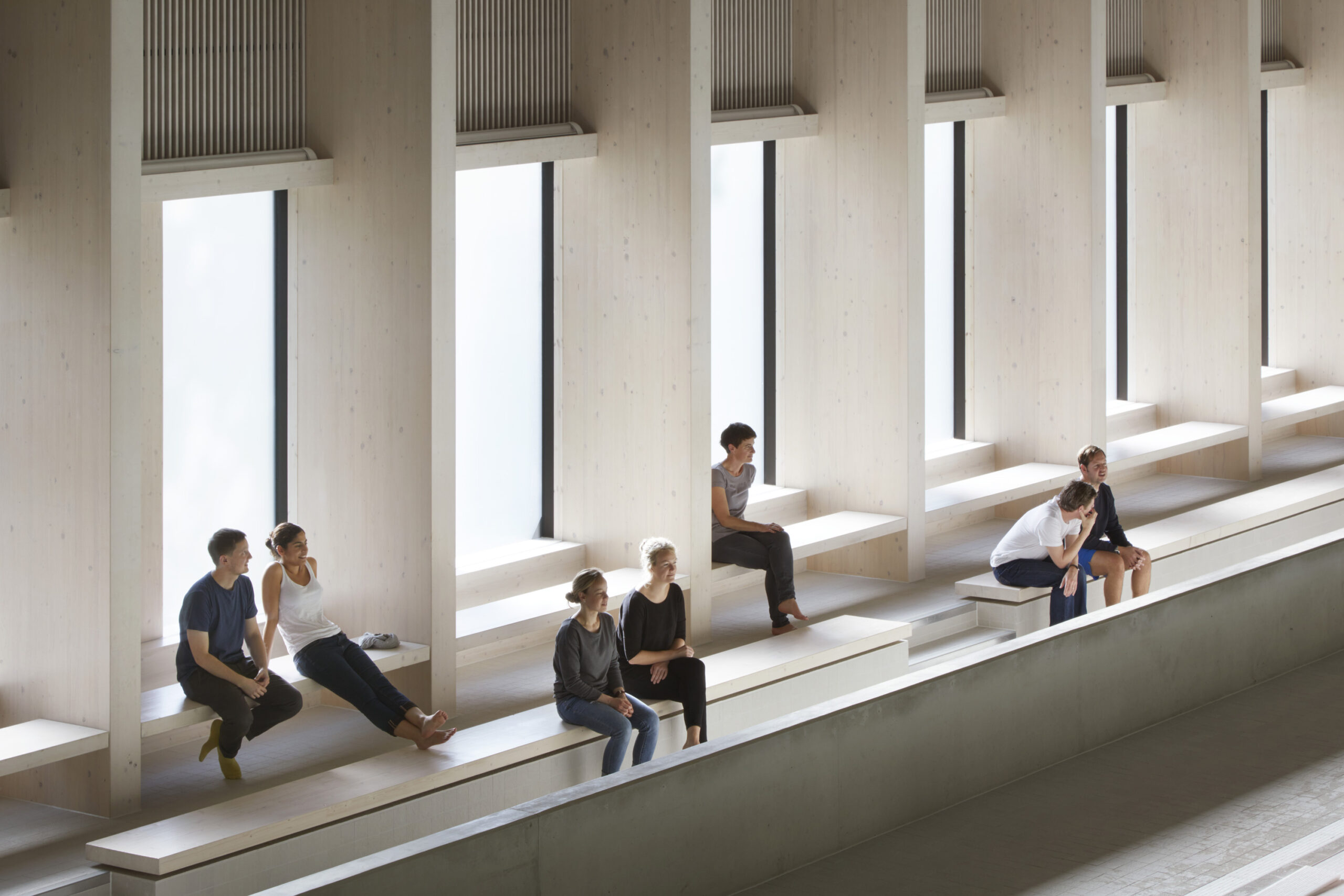 Interior shot of people sat down on the benches next to the City of London Freemen's School Swimming Pool.