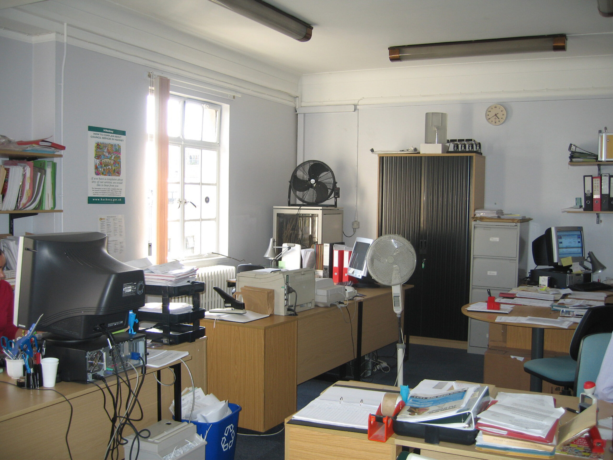 Interior shot showing the workspace before the refurbishment, - a cluttered office, with documents and computers