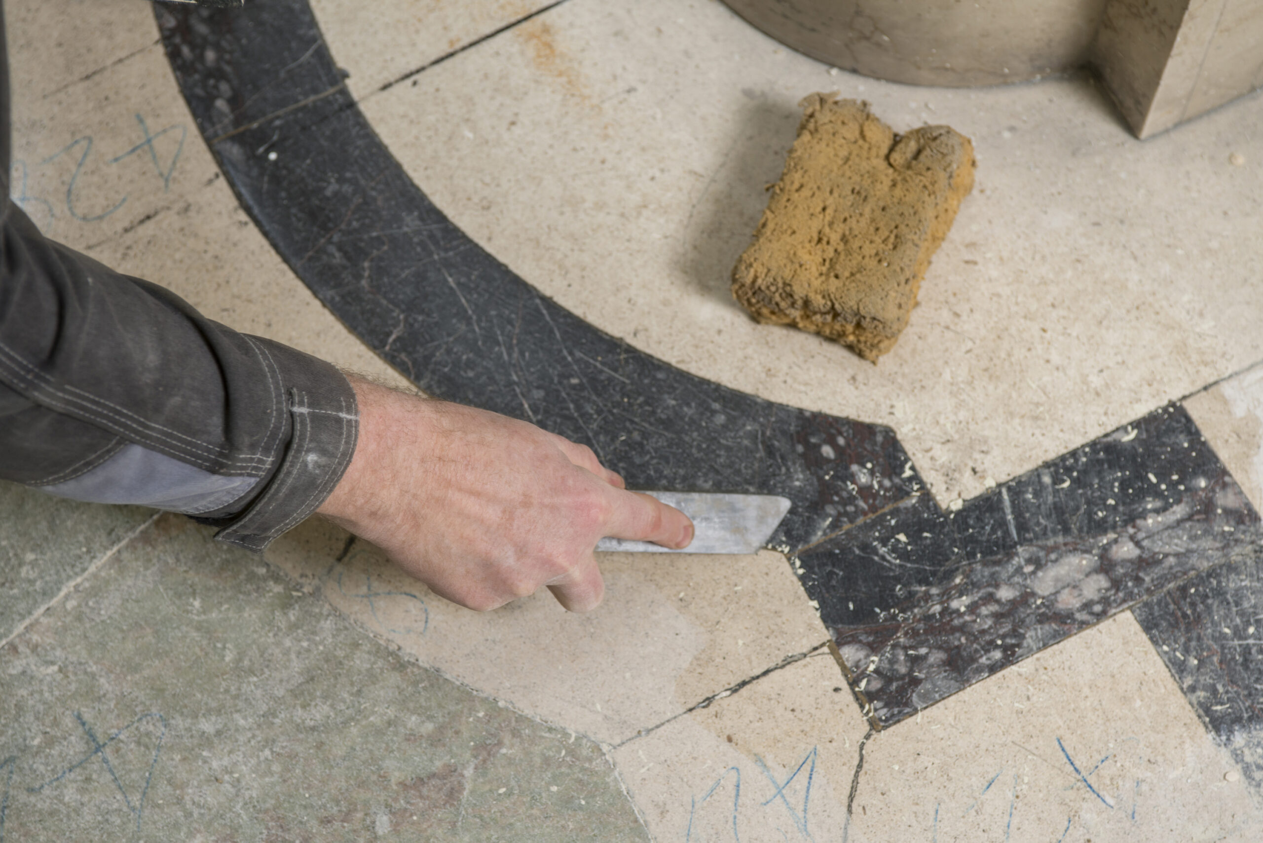 Interior close up showing a craftsmen working on the tiling on the floor.