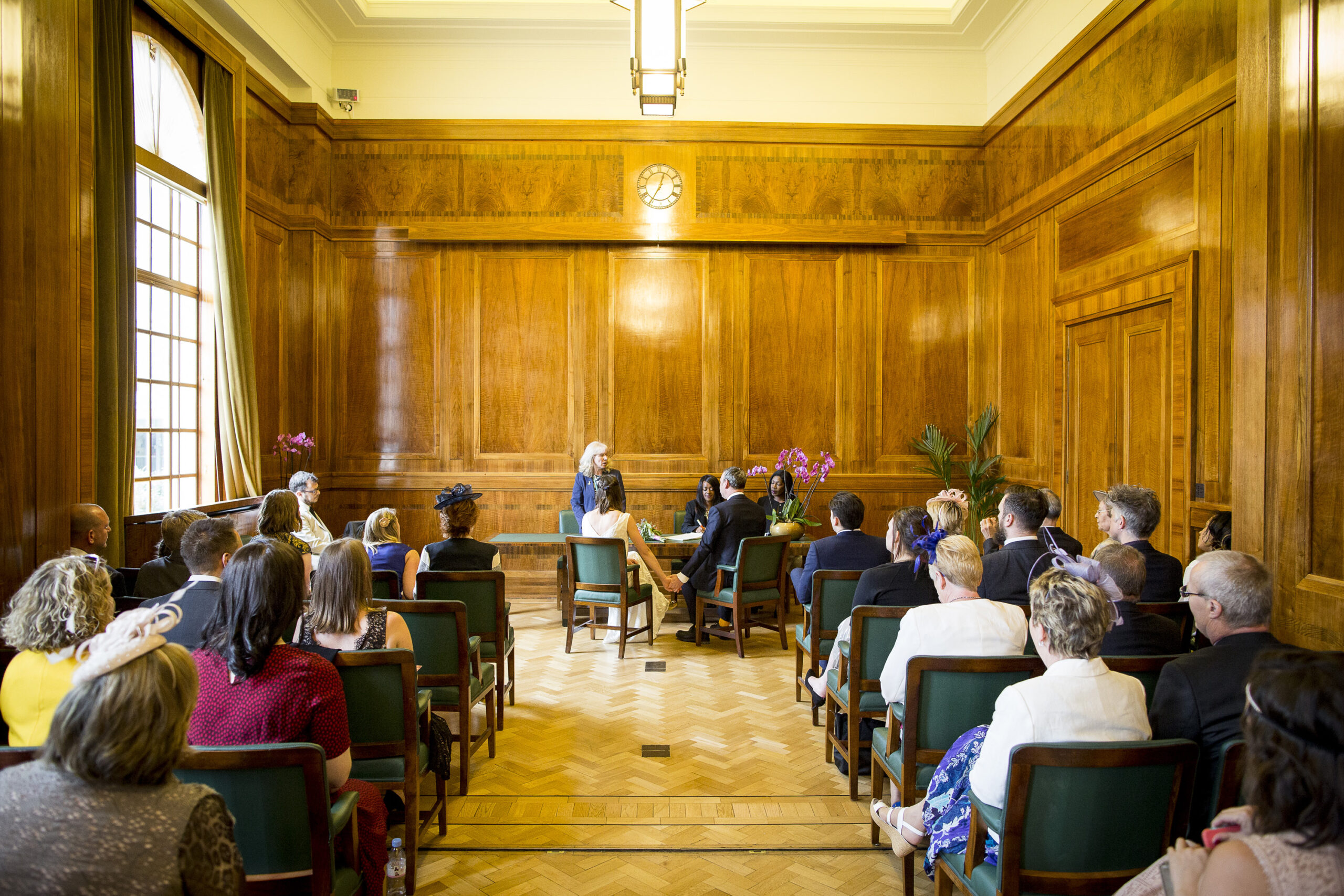 Interior shot of a wedding suite, filled with people watching a wedding ceremony at Hackney Town Hall
