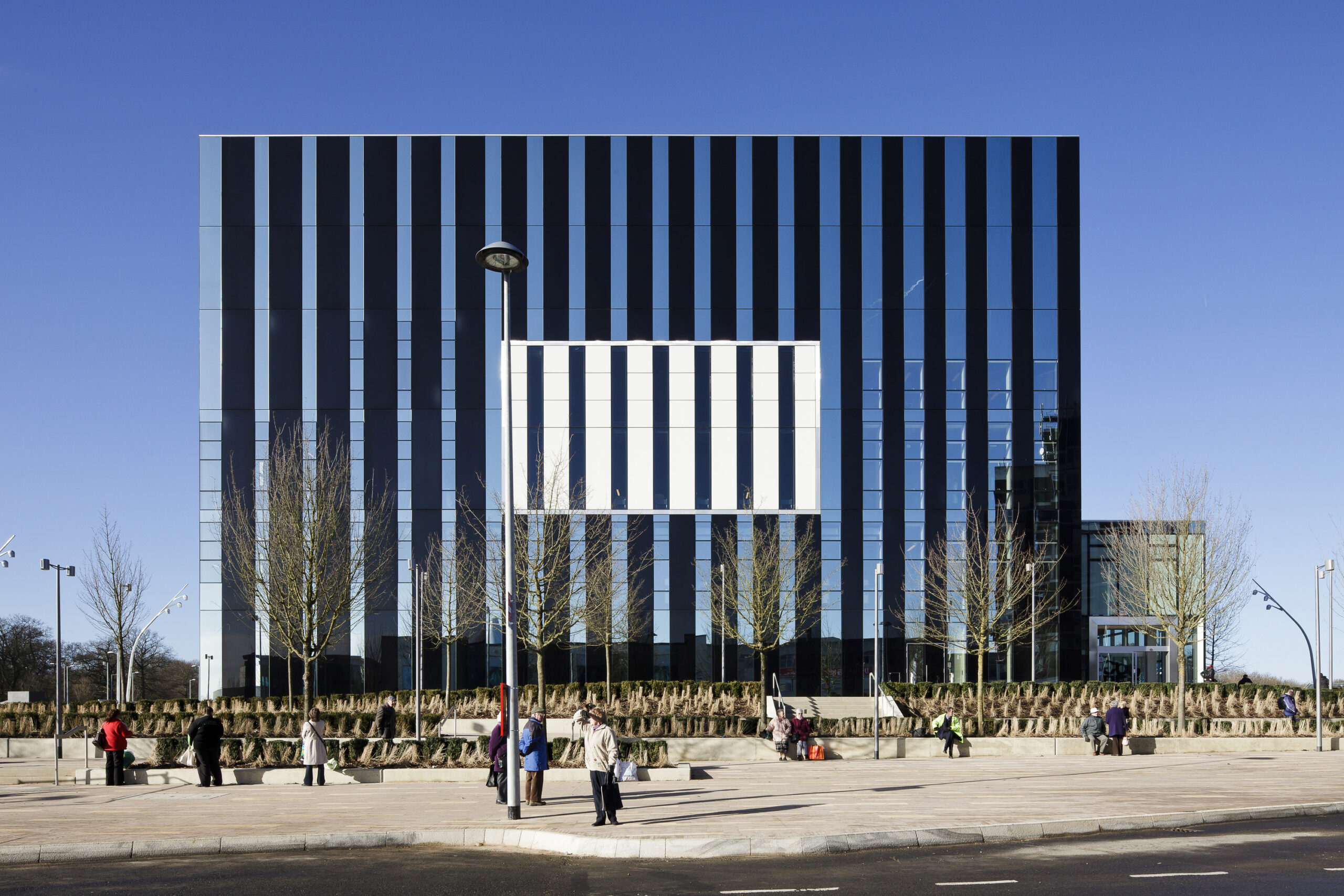 Street view of the people standing at the bus stop outside of the Corby Cube